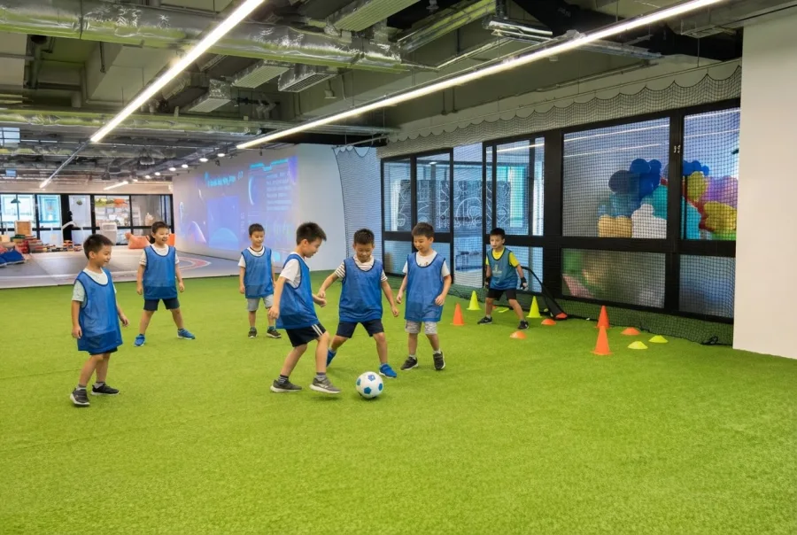 Young children in blue bibs playing on the indoor turf pitch at MosKiddo